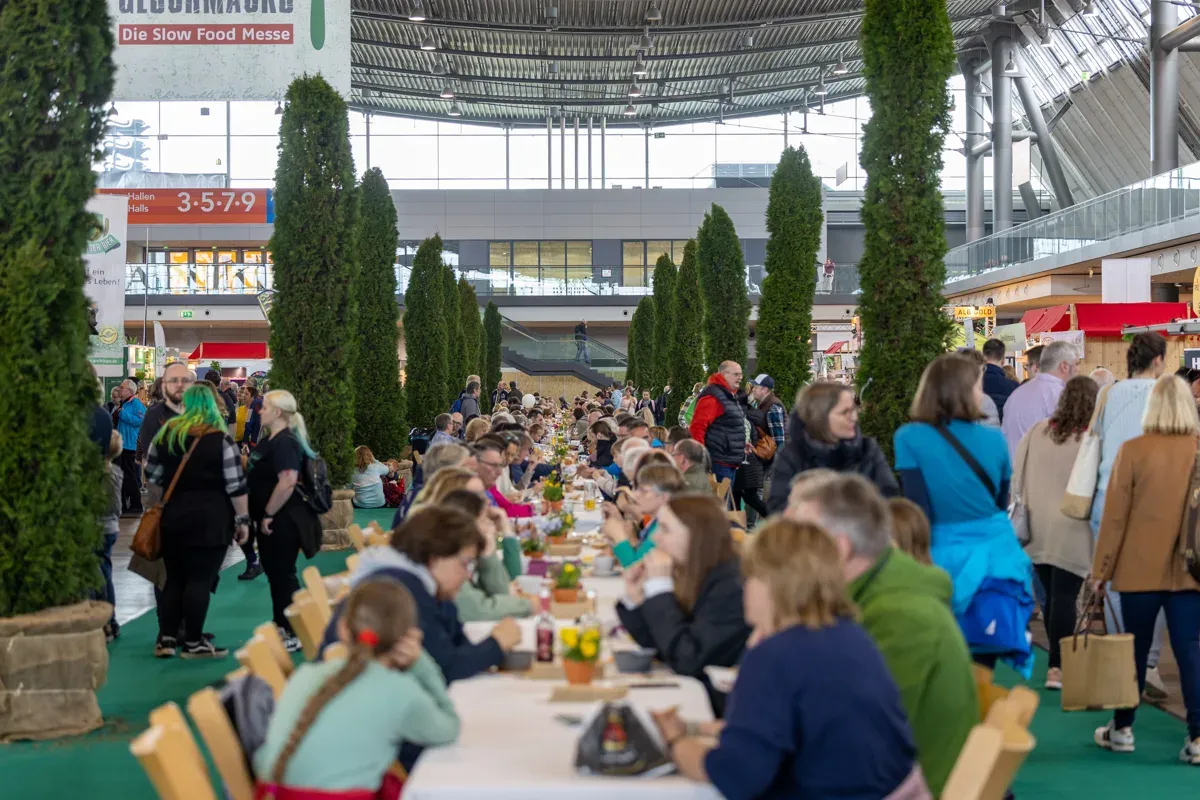 Lange Tafel beim „Markt des guten Geschmacks“ auf der Slow Food Messe: Mit Tischnachbarn ins Gespräch kommen und dabei regionale Spezialitäten genießen.